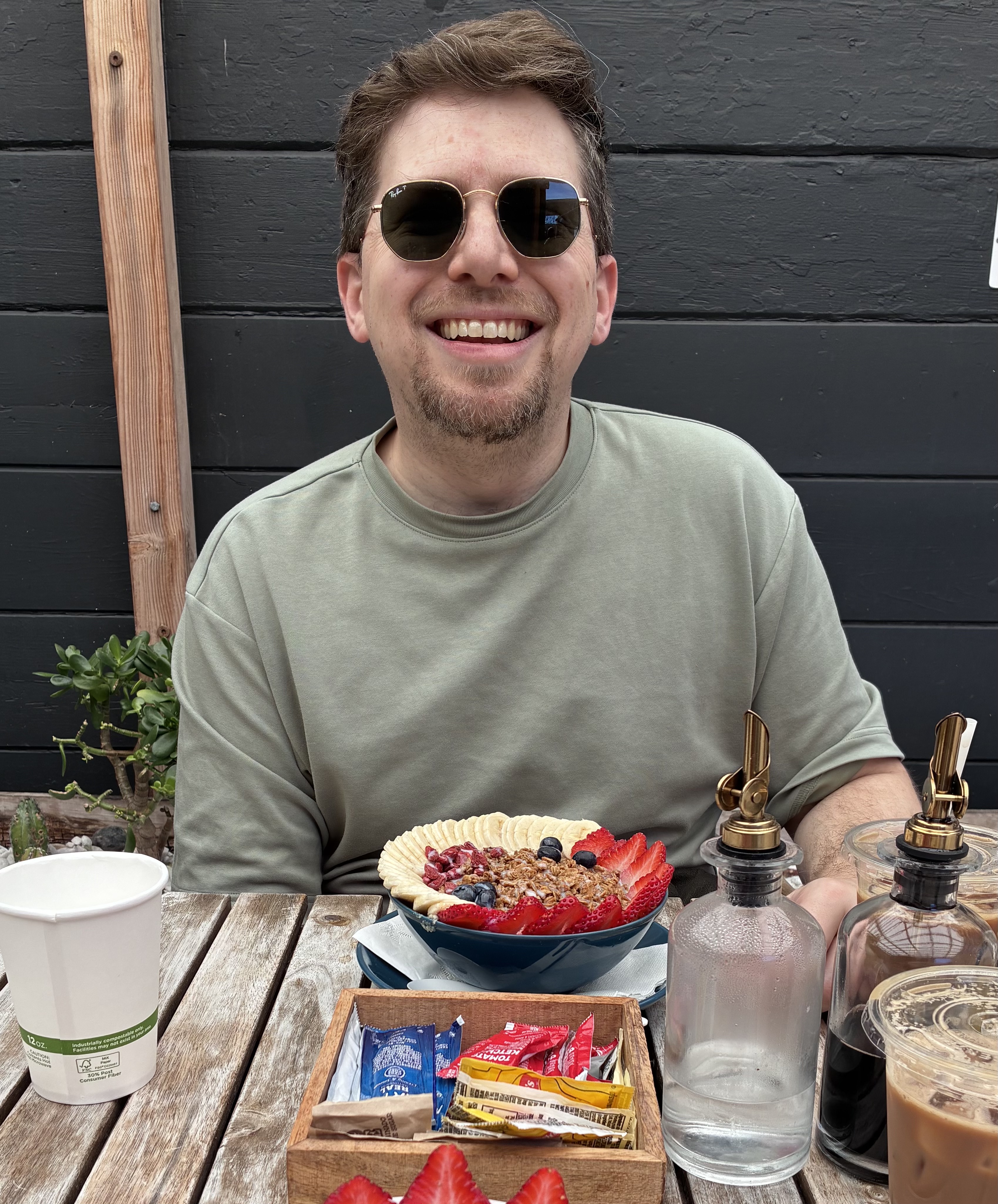 Danny smiling at an outdoor cafe table in sunglasses, with an açaí bowl in front of him